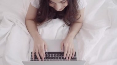 Yatak odasında yatağın üstüne yalan sırasında bilgisayar veya dizüstü bilgisayar kullanarak güzel Asya mix yarış beyaz bir kadın. Mutlu kadın evde alışveriş online satın alma. Evde kavramı rahatlatıcı yaşam tarzı kadın.