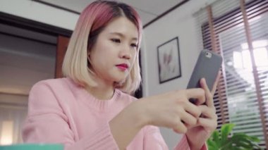 Güzel Asyalı kadın Danışma onun oturma odasında yatarken Smartphone kullanarak. Mutlu erkek okuma, mesajlaşma ve evde online satın alma telefon mesaj attığın için kullanın. Yaşam tarzı kadına ev concept.