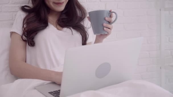 美丽迷人的亚洲妇女的肖像使用电脑或膝上型电脑 当躺在床上时 在她家的卧室里放松的时候 拿着一杯温暖的咖啡或茶 生活方式妇女在家庭概念 — 图库视频影像