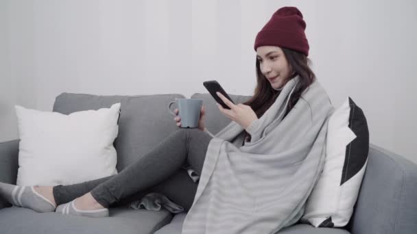 美丽迷人的亚洲妇女使用智能手机的短信和阅读 而躺在沙发上时 在家里的客厅放松 家庭生活中的女性在圣诞节和新年假期的概念 — 图库视频影像