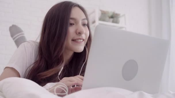 コンピューターまたはラップトップを使用して美しい魅力的なアジア女性の肖像とベッドの上に横たわっている間音楽を聴くとき 自宅に彼女の寝室でリラックスします ライフ スタイルの女性使用リラックス ホーム コンセプト時 — ストック動画