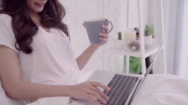 Bilgisayar ya da laptop sıcak bir fincan kahve ya da çay yatakta yatıyordu süre tutarak kullanan güzel çekici Asyalı kadın portresi ne zaman evde yatak odasında rahatlayın. Yaşam tarzı kadınlara ev concept.