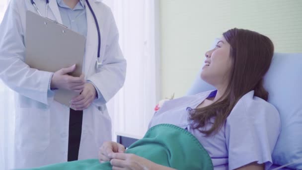 美しいスマート アジア医師と患者の病院で患者さんのベッドに滞在しながら医師の手でクリップボードに何かを説明します 医学と医療の概念 — ストック動画