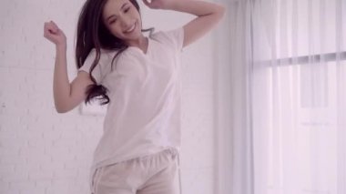 Neşeli mutlu Genç Asyalı kadın kulaklıklarla dans ederken yatak yatak odasında müzik dinleme. Yaşam tarzı kadın dinlenmek evde.