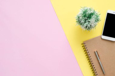 Ofis Masası adlı kullanıcının alanı - düz çalışma beyaz boş defter sayfası, ağaç bitki ve sahte telefon pastel arka plan üzerinde bir çalışma alanının en iyi görünümü yatırın. Pastel pembe sarı renk arka plan boşluk kavramı.