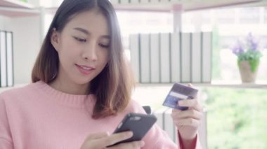 Güzel Asyalı kadın Smartphone Resepsiyon evde oturma odasında oturup giyim kazak sırasında kredi kartıyla alışveriş online satın alma kullanarak. Yaşam tarzı kadına ev concept.