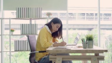 Asyalı kadın çalışma dizüstü evde oturma odasında masa üzerinde gülümseyen güzel genç. Asya iş kadını defter belge finans ve hesap makinesi ev ofis yazma. Ev concept anda zevk.