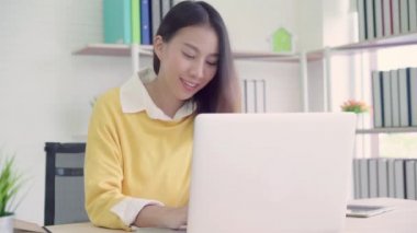 Asyalı kadın çalışma dizüstü evde oturma odasında masa üzerinde gülümseyen güzel genç. Asya iş kadını defter belge finans ve hesap makinesi ev ofis yazma. Ev concept anda zevk.