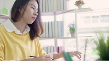Asyalı kadın çalışma dizüstü evde oturma odasında masa üzerinde gülümseyen güzel genç. Asya iş kadını defter belge finans ve hesap makinesi ev ofis yazma. Ev concept anda zevk.