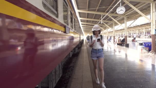 慢动作 旅行者背包客亚洲妇女旅行在曼谷 愉快的年轻女性使用智能手机聊天 阅读和短信在火车站 — 图库视频影像