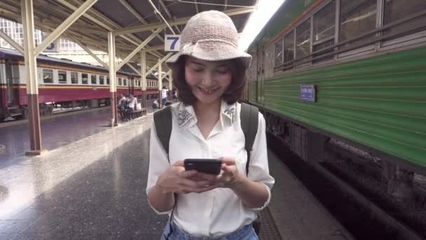 スローモーション 旅行バックパッカー アジア女性はタイのバンコクに旅行します 話して 読んで 駅でテキスト メッセージのスマート フォンを使用して幸せな若い女性 — ストック動画