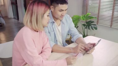 Genç Asyalı aile çift haber tartışmaya veya online alışveriş birlikte masanın üzerinde evde hafta sonu birlikte oturan yapıyor tablet, ciddi erkek ve kadın için yeni satış teklifleri web arama tarama kullanarak.