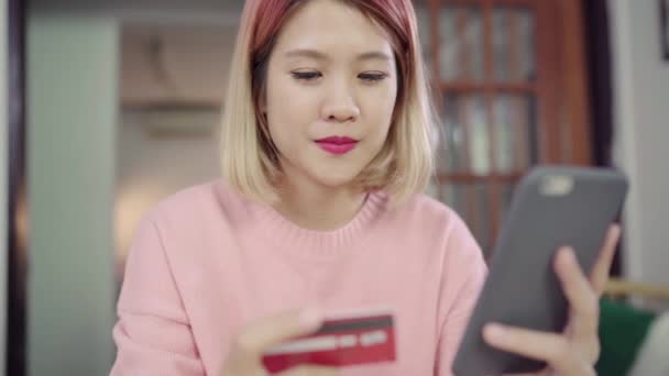 美丽的亚洲妇女使用智能手机购买信用卡网上购物 而穿毛衣坐在办公桌上的客厅在家里 生活方式妇女在家的概念 — 图库视频影像