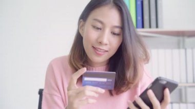 Güzel Asyalı kadın Smartphone Resepsiyon evde oturma odasında oturup giyim kazak sırasında kredi kartıyla alışveriş online satın alma kullanarak. Yaşam tarzı kadına ev concept.