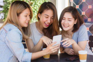 Arkadaş grubu kahve içme ve birlikte konuşurken kafede oturan neşeli Asyalı Genç kadınlar. Kahve için konuşma, okuma ve manifatura smartphone kullanırken zevk çekici Asyalı kadın.