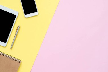 Ofis Masası adlı kullanıcının alanı - düz çalışma boş defter sayfası ve boş boş sahte telefon tablet pastel arka plan üzerinde yukarı çalışma alanının en iyi görünümü yatırın. Pastel pembe sarı renk arka plan boşluk kavramı.