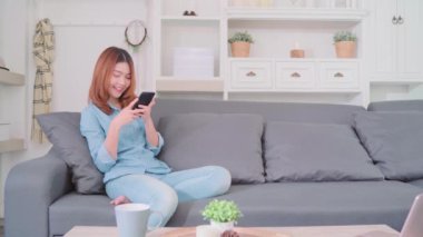 Kanepede yatan smartphone kullanarak güzel çekici genç gülümseyen Asyalı kadın portresi ne zaman evde oturma odasında gevşeyin. Ev concept zaman yaşam tarzı kadınlar enjoying.