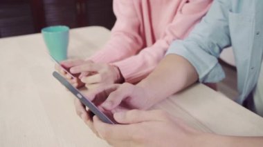Genç Asyalı aile çift haber tartışmaya veya online alışveriş birlikte masanın üzerinde evde hafta sonu birlikte, ciddi erkek ve kadın için yeni satış teklifleri web arama tarama oturan yapıyor smartphone kullanarak.