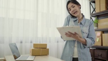 Akıllı Asya iş kadın sahibi KOBİ online telefon kullanarak stoktaki müşteri kontrol ürün almak ve Pano evde çalışma hakkında yazmak. Küçük işletme sahibi, ev ofis kavramı.