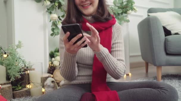 快乐快乐的年轻亚洲女性在圣诞节期间 用智能手机在家里的客厅里查看社交媒体 生活方式女性庆祝圣诞节和新年概念 — 图库视频影像