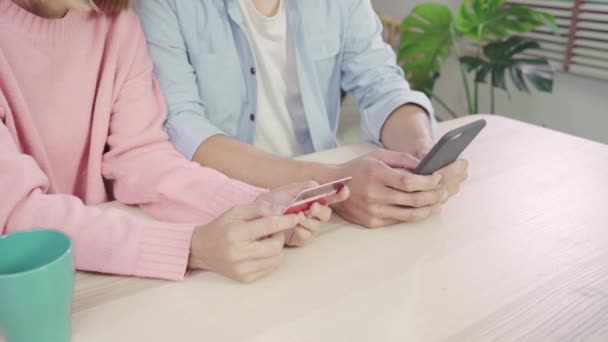 年轻的亚洲家庭夫妇使用智能手机讨论新闻或做网上购物坐在一起在办公桌上在家里周末 认真的男人和女人浏览网页搜索新的销售优惠 — 图库视频影像