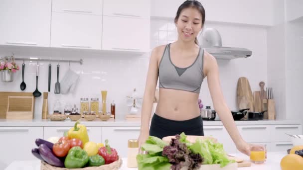 Die junge Asiatin tanzt fröhlich, hört Musik, trinkt Orangensaft und kocht zu Hause in der Küche in Sportkleidung Salat. Lifestyle Frauen machen gesundes Ernährungskonzept.