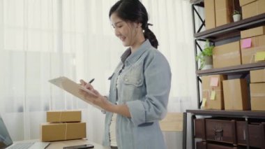 Akıllı Asya iş kadın sahibi KOBİ online telefon kullanarak stoktaki müşteri kontrol ürün almak ve Pano evde çalışma hakkında yazmak. Küçük işletme sahibi, ev ofis kavramı.