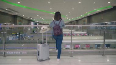 Birçok bagajlı terminal salonunda Uluslararası Havaalanı kalkış kapısında yatılı uçuşa giderken yürüme arabası veya sepeti kullanarak mutlu Asyalı kadın. Kadınlar Havaalanı kavramında mutlu.
