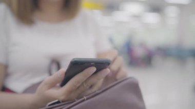 Kullanarak ve onun smartphone uçağının kalkış kapısı uluslararası havaalanında beklerken terminal Salonu sandalyede oturan süre kontrol mutlu Asyalı kadın. Kadınlar Havaalanı kavramında mutlu.