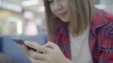 Kullanarak ve onun smartphone uçağının kalkış kapısı uluslararası havaalanında beklerken terminal Salonu sandalyede oturan süre kontrol mutlu Asyalı kadın. Kadınlar Havaalanı kavramında mutlu.