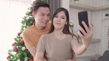 Akıllı telefon selfie ile Noel ağacı kullanarak Asya çift Noel Festivali evde onların oturma odası süslemeleri. Yaşam tarzı kadın ve adam mutlu yaz kutlamak Noel ve yeni yıl kavramı.
