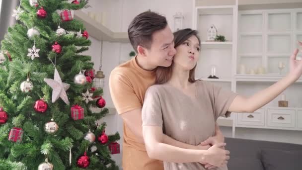 アジアのカップルのクリスマス ツリーでスマート フォン Selfie を使用して自宅クリスマス フェスティバルで彼らの居間を飾る ライフ スタイルの女と男の幸せな夏を祝うクリスマスと新しい年の概念 — ストック動画