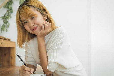 Asyalı kadın yazma alışveriş mutfak tezgahı evde ve okuma kalem tarafından Not Defteri'nde listeler ve alışverişe için tüm malzemeyi hatırlamaya çalışır. Yaşam tarzı kadın evde kavramı relax.
