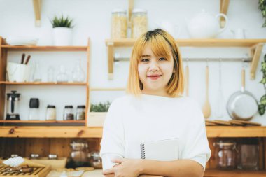 Asyalı kadın yazma alışveriş mutfak tezgahı evde ve okuma kalem tarafından Not Defteri'nde listeler ve alışverişe için tüm malzemeyi hatırlamaya çalışır. Yaşam tarzı kadın evde kavramı relax.