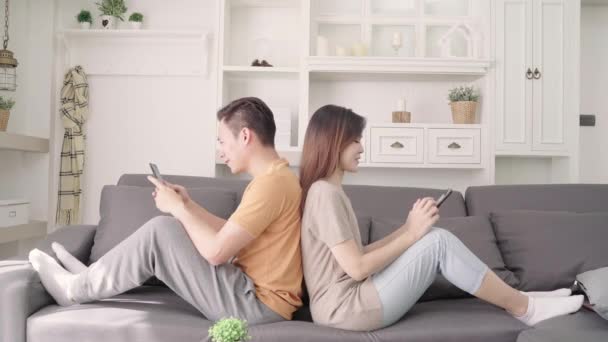 アジアのカップルは 自宅のリビング ルームでスマート フォン チェック ソーシャル メディアを使用して 甘いカップルは ソファの上に横たわっている間愛の瞬間を楽しむ家でくつろぐとき ライフ — ストック動画