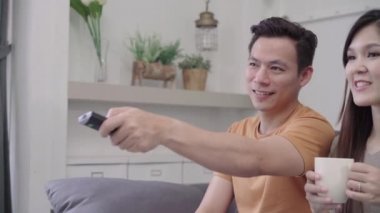 Asya çift, TV izlerken ve sıcak fincan kahve oturma odasında evde içme tatlı çift kanepede yatarken aşk keyfini ne zaman evde dinlenin. Yaşam tarzı çift evde kavramı relax.