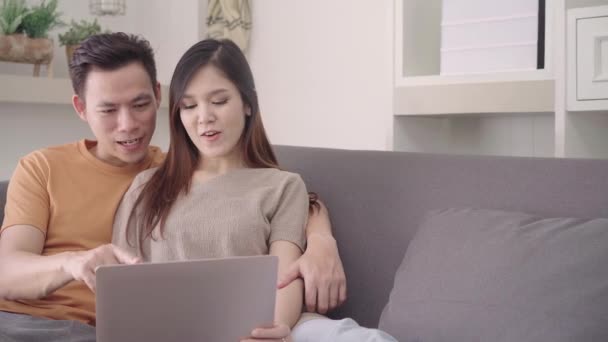 亚洲夫妇使用笔记本电脑在家里的客厅搜索网络 甜蜜的夫妇享受爱的时刻 而躺在沙发上放松在家 生活方式夫妇在家里放松的概念 — 图库视频影像