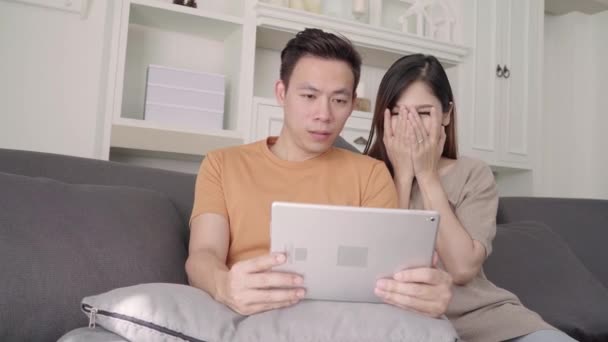 亚洲夫妇在家里客厅里用平板电脑上网购物 甜蜜的夫妇在家里放松的时候躺在沙发上享受爱情的时刻 生活方式夫妻在家里放松一下 — 图库视频影像