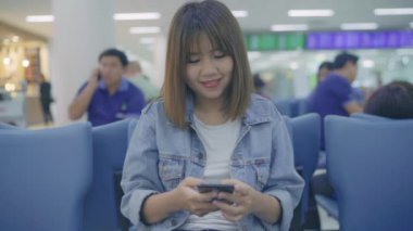 Yavaş hareket - kullanarak ve uçağının kalkış kapısı uluslararası havaalanında beklerken onun smartphone terminal salonunda kontrol mutlu Asyalı kadın. Kadınlar Havaalanı kavramında mutlu.