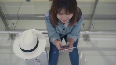 Kullanarak ve onun smartphone uçağının kalkış kapısı uluslararası havaalanında beklerken terminal Salonu sandalyede oturan süre kontrol mutlu Asyalı kadın. Kadınlar Havaalanı kavramında mutlu.