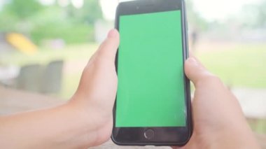 Genç Asyalı kadın ile yeşil ekran siyah cep telefonu cihaz kullanarak. Kafede otururken sayfalarını kaydırma Asyalı kadın smartphone, holding. Chroma anahtar.