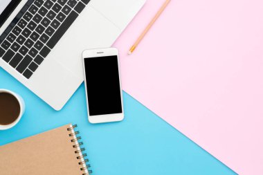 Yaratıcı düz Fotoğraf çalışma masası yatıyordu. Üstten görünüm ofis masası mavi pembe renkli arka plan üzerinde dizüstü bilgisayar, telefon, kalem, defter ve kahve Kupası ile. Kopya alanı, düz yatıyordu fotoğraf ile üstten görünüm.