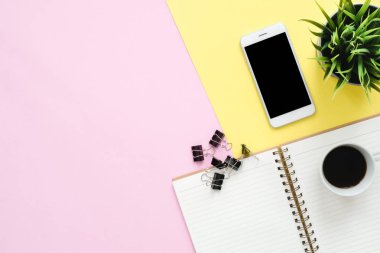 Ofis Masası adlı kullanıcının alanı - düz çalışma beyaz boş defter sayfası, kahve fincanı ve sahte telefon pastel arka plan üzerinde bir çalışma alanının en iyi görünümü yatırın. Pastel pembe sarı renk arka plan boşluk kavramı.