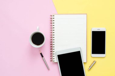 Ofis Masası adlı kullanıcının alanı - düz çalışma boş defter sayfası, kahve fincanı ve sahte telefon tablet pastel arka plan üzerinde yukarı çalışma alanının en iyi görünümü yatırın. Pastel pembe sarı renk arka plan boşluk kavramı.