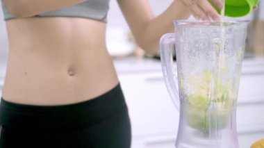 Yavaş hareket - Sportif Asyalı kadın mutfakta, güzel erkek spor giyim kullanım organik meyve birçok beslenme kendini evde elma suyu yapmak blender kullanarak. Sağlıklı gıda kavramı.