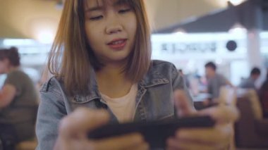 Kullanarak ve onun smartphone uçağının kalkış kapısı uluslararası havaalanında beklerken terminal Salonu sandalyede oturan süre kontrol mutlu Asyalı kadın. Kadınlar Havaalanı kavramında mutlu.