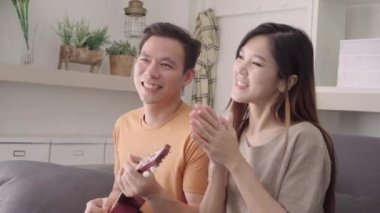 Gitar çalmak ve birlikte şarkı evde oturma odasında Asya çift, tatlı çift kanepede yatarken aşk keyfini ne zaman evde dinlenin. Yaşam tarzı çift evde kavramı relax.