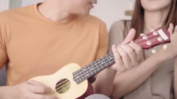 亚洲夫妇在家里的客厅里一起弹吉他和唱歌 甜蜜的情侣们在家里放松的时候躺在沙发上享受爱情时刻 生活方式夫妇在家里放松的概念 — 图库视频影像
