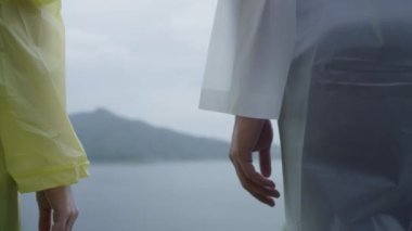 Genç Asyalı tatlı çift romantik zaman göl kenarında yağmurluk ayakta giyerken yağmur oynayan kullanarak mutlu hissediyor. Yaşam tarzı çift zevk ve yağmurlu günde dinlenmek.