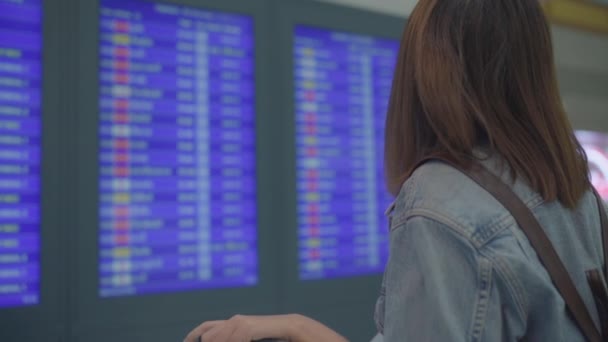 慢动作 快乐的亚洲妇女看着信息板检查她的航班与行李在候机楼在国际机场的登机口 生活中的女人快乐在机场概念 — 图库视频影像